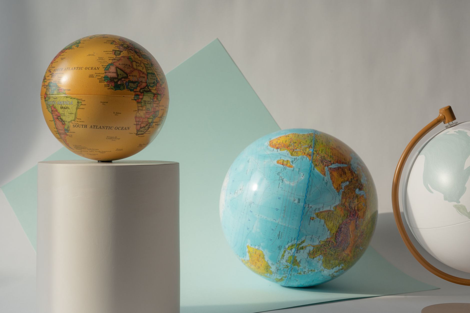 Colorful globes displayed artistically on white cylinders with soft pastel backgrounds.