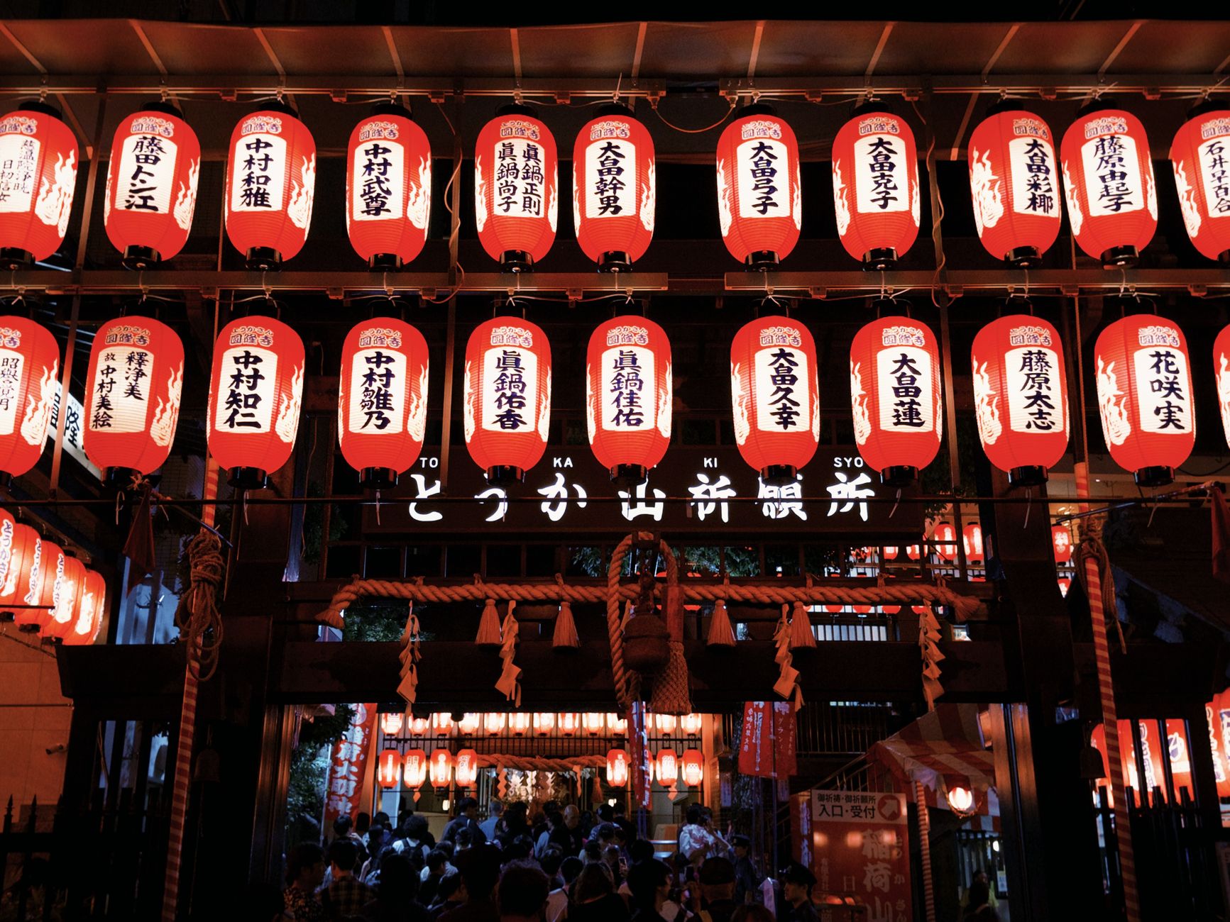 Colorful Japanese lanterns illuminate a bustling street festival during the night.