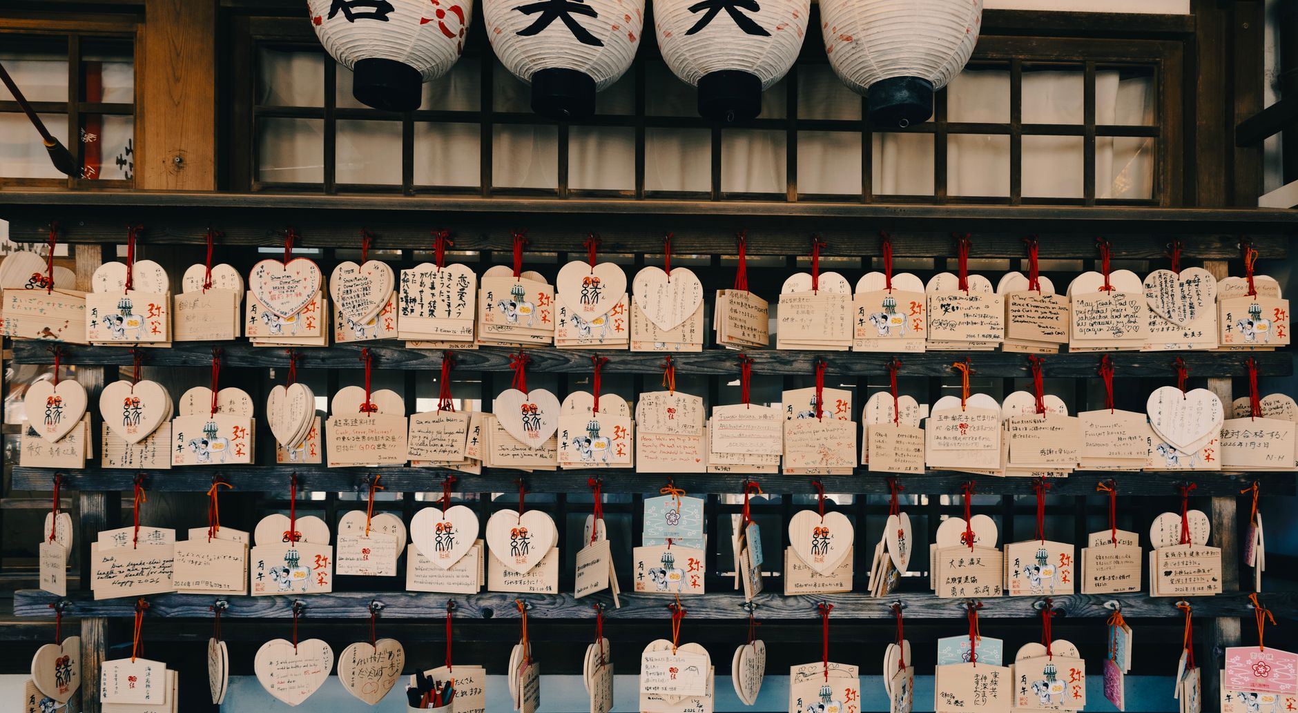 Heart-shaped wooden ema tablets with handwritten wishes hanging at a Japanese shrine.