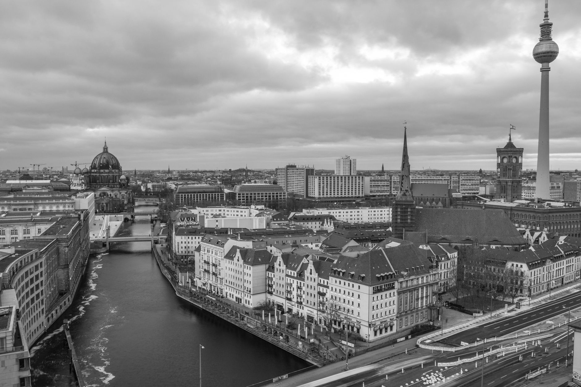 A dramatic black and white aerial view of Berlin featuring the iconic Fernsehturm and Spree River.