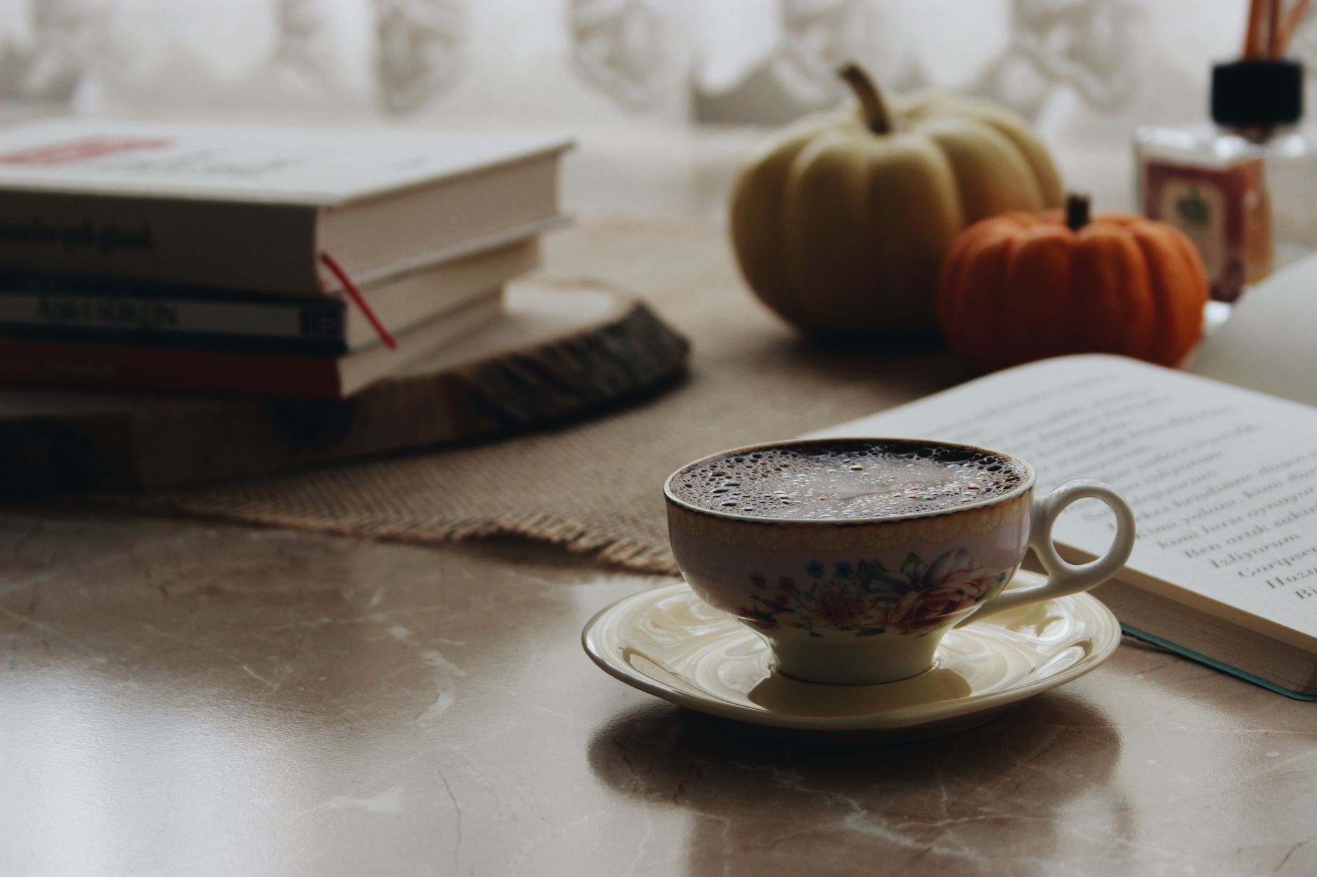 A warm cup of coffee with books and pumpkins on a cozy indoor table setting.
