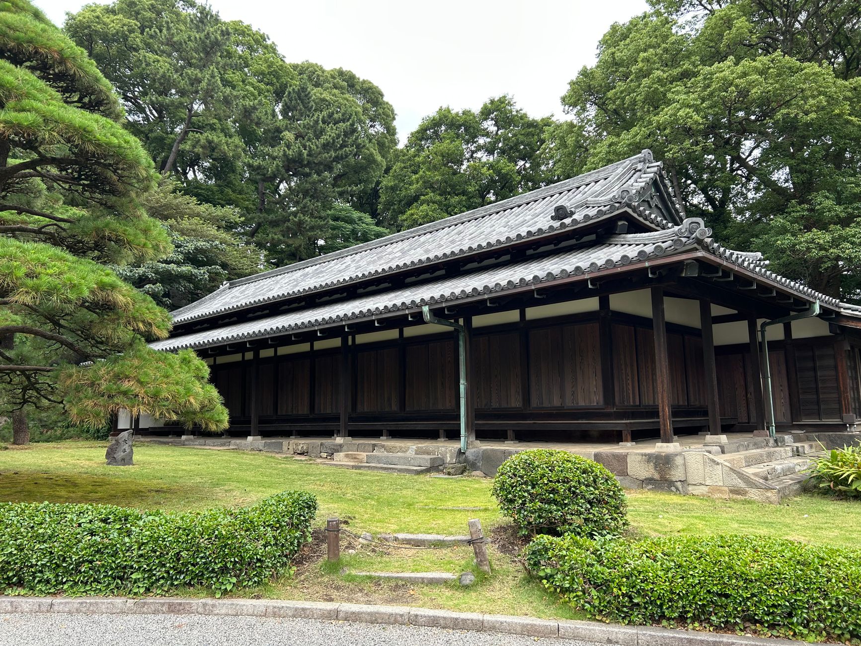 A historic Japanese timber building surrounded by lush greenery in a tranquil garden.