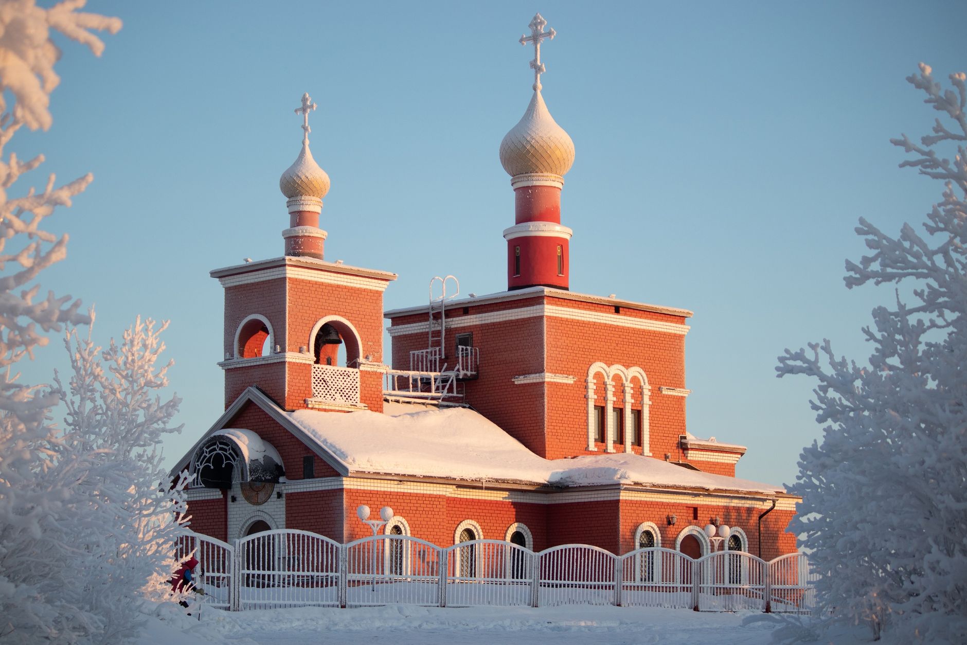 Beautiful red-brick church with domes covered in snow amidst a clear winter sky.