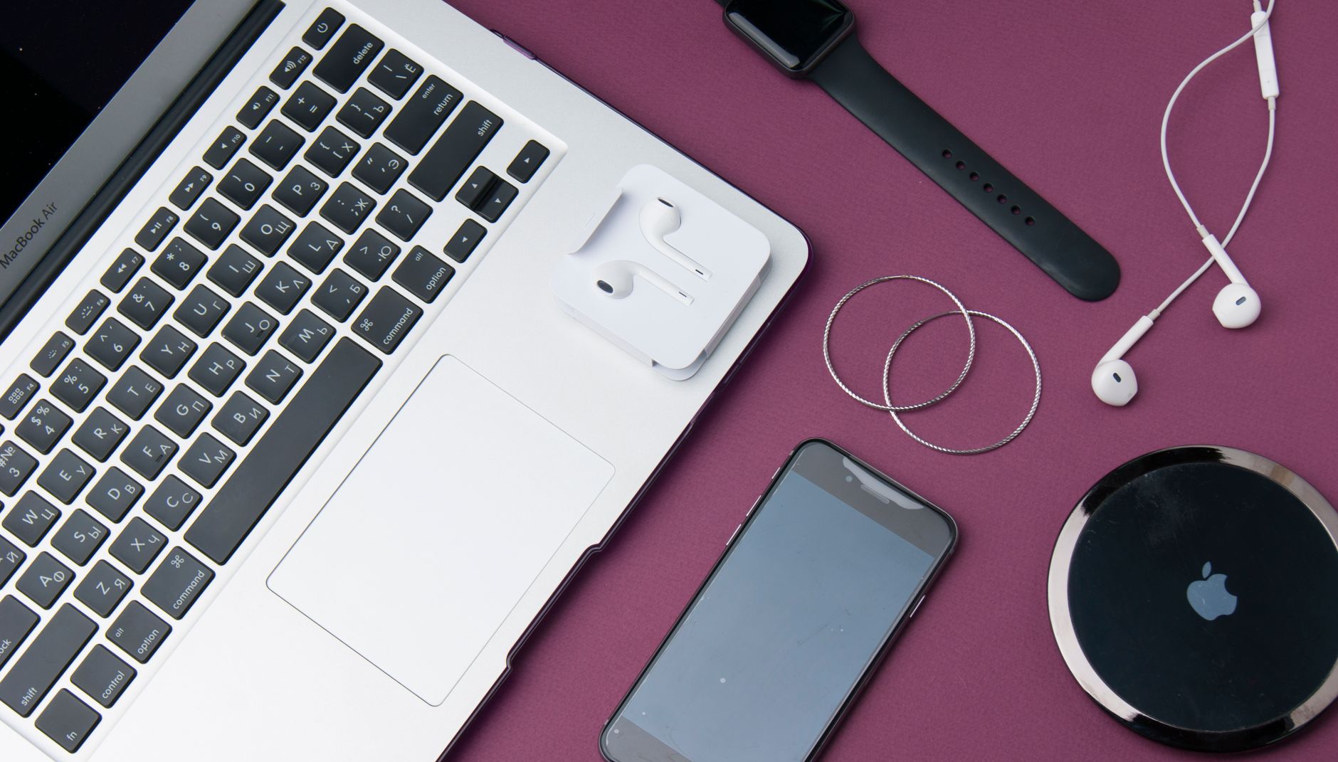 Flat lay of various electronic gadgets on a purple surface including a laptop, smartphone, and smartwatch.