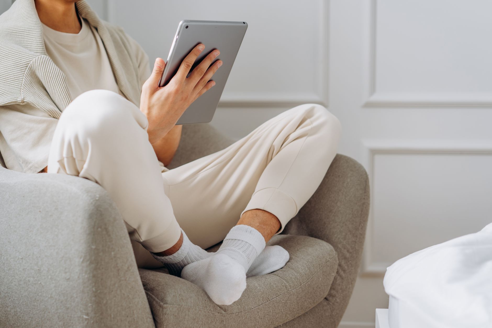 Adult relaxing indoors with a tablet, dressed in casual home attire, sitting comfortably on a chair.
