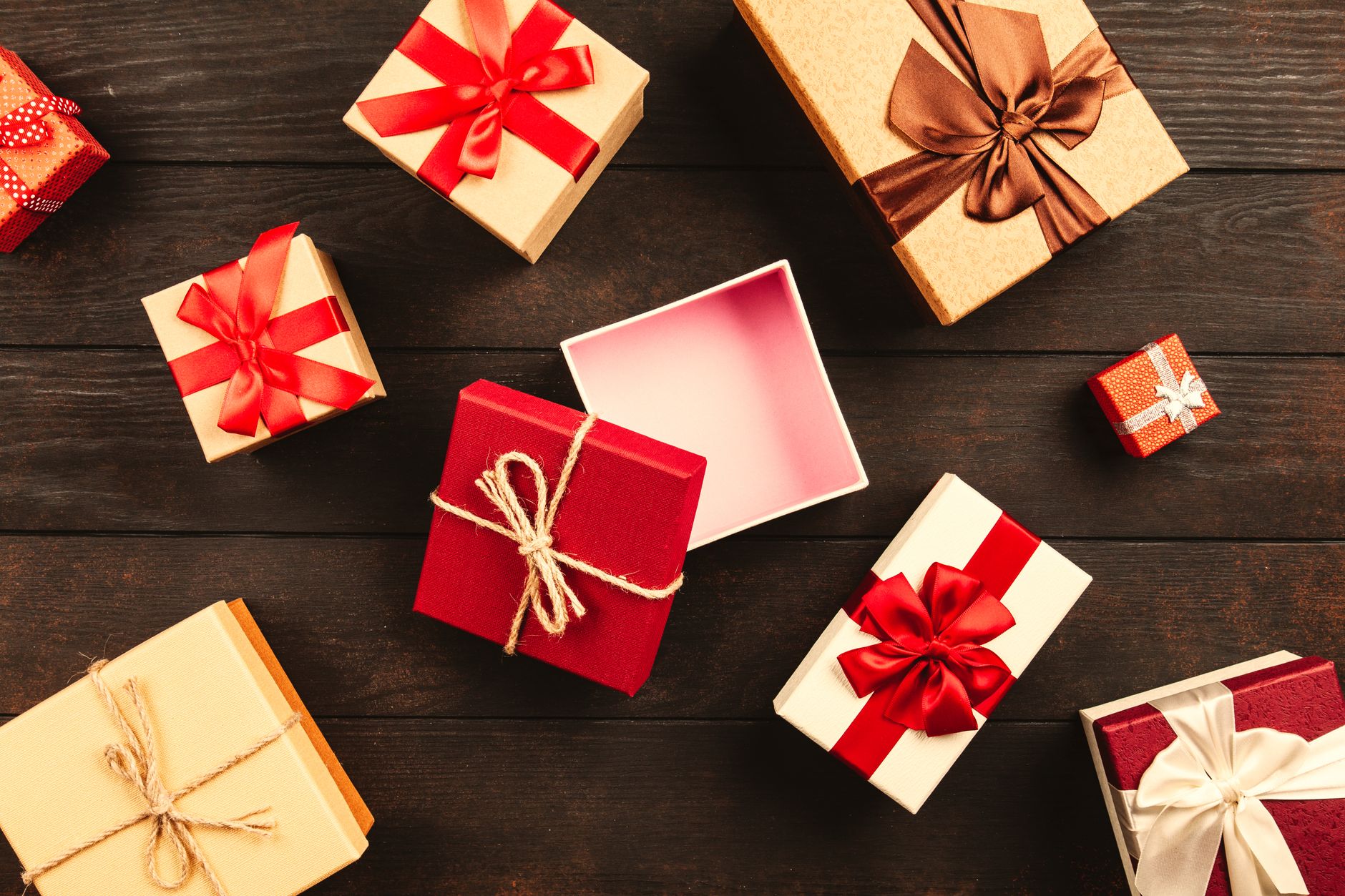 A festive flat lay of various Christmas presents adorned with colorful ribbons on a wooden background.