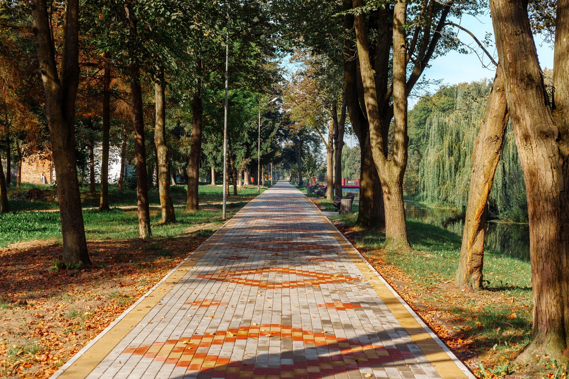 A peaceful park pathway lined with trees, featuring vibrant autumn leaves and a clean stone path.